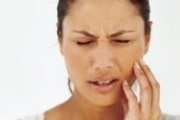 A woman with jaw pain winces winces and touches her cheek