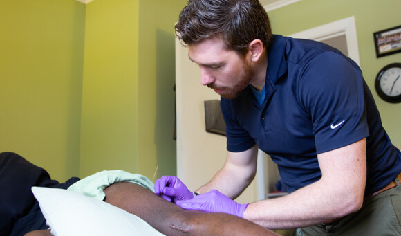 A physical therapist performs dry needling on a patient focusing on the arm