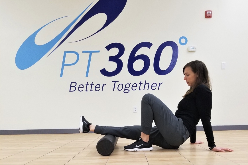 A woman uses a foam roller under her leg in a PT360 workout room