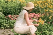 A woman in a floppy hat tend to flowers in a garden