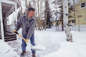 A photo of a man shoveling snow from the walk in front of a house